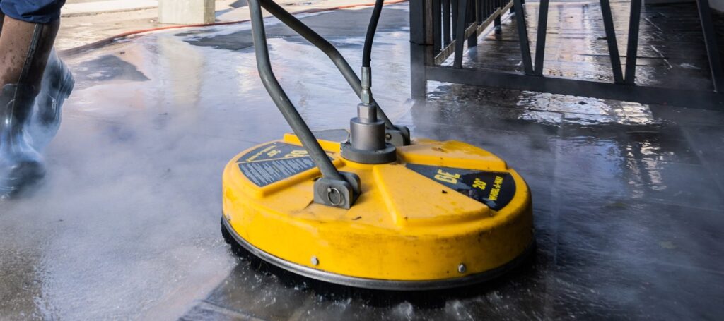 Professional flat surface cleaner spraying a wet outdoor paved surface, mist rising, during pressure washing (illustrative stock photo, not a Watermark job)