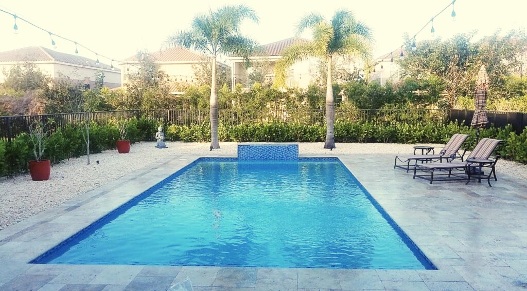 Rectangular pool with raised spa and fountain on a travertine paver deck